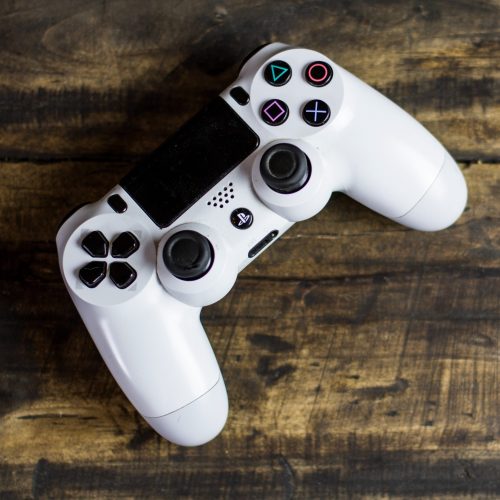 A white PlayStation controller sits atop a wooden table.