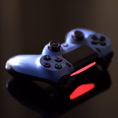 A blue PlayStation controller with a glowing red light sits atop a table.